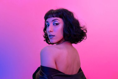 Sırtı çıplak genç bir kadın dönüp kameraya bakıyor. Gülümseyen modern kadın portresi moda görünümlü ve parlak renklerde..