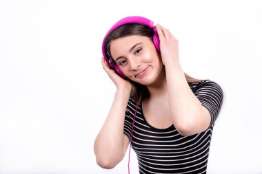 Uzun saçlı, gülümseyen güzel bir kızın portresi. Genç kadın kot pantolon ve çizgili gömlek giyiyor ve müzik dinlemek için kulaklık kullanıyor..