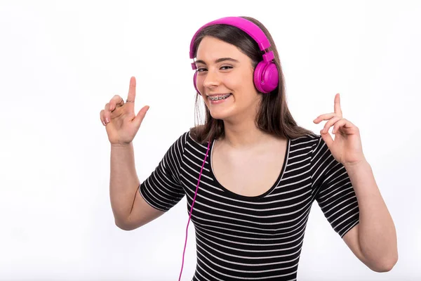 Uzun saçlı, gülümseyen güzel bir kızın portresi. Genç kadın kot pantolon ve çizgili gömlek giyiyor ve müzik dinlemek için kulaklık kullanıyor..