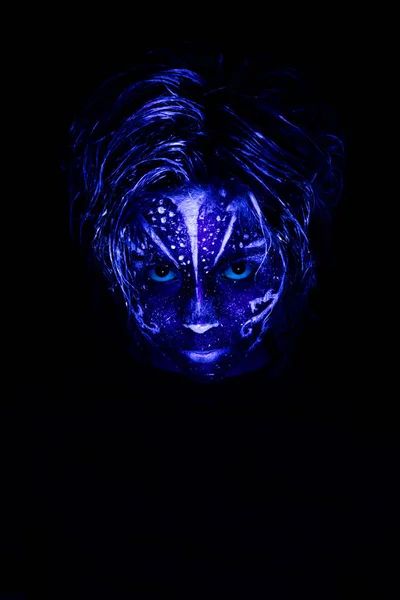 Young girl made up with fluorescent colors. Portrait of a beautiful girl with tribal designs illuminated by ultraviolet black light.