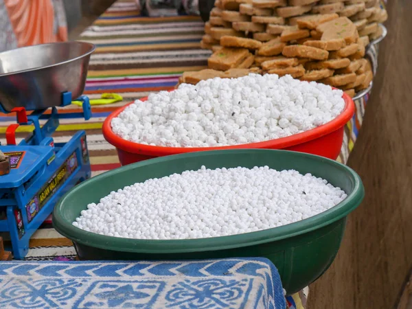 Pushkar, Rajasthan / Hindistan - 5 Kasım 2019: Hint sokak yemekleri satıcısı Nokuldana ve yiyecek ürünlerini sokak pazarında satıyor. Nakul Dana, ayrıca Ram Dana ve Mimosa şeker topları olarak da bilinir..