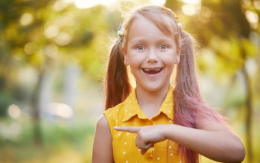 Dişsiz çocuklar gülümser. Küçük tatlı kız gülüyor, ilk süt dişini gösteriyor. Çocuk dişçiliği. Neşeli çocuk solu işaret ediyor