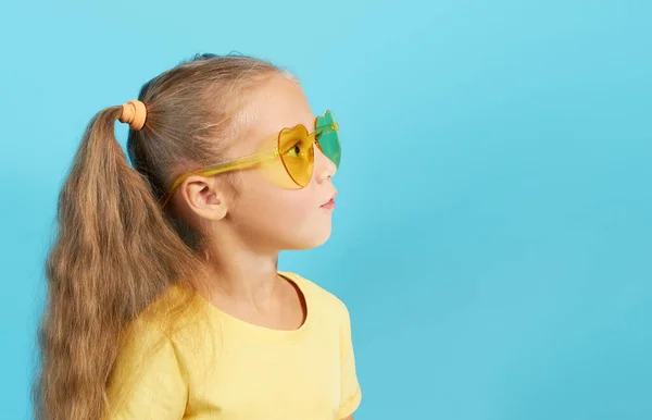一个可爱的小女孩 头戴黄色眼镜 头戴黄色T恤 发型开朗 她的右边是蓝色背景 空白的登记空间 — 图库照片
