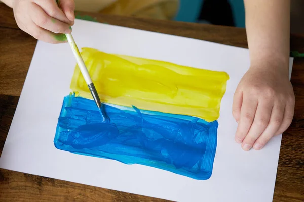 Sad child girl draws a picture of the war in Ukraine. Bright drawing with colors of the State flag of Ukraine, yellow and blue. Stop the war, save the world
