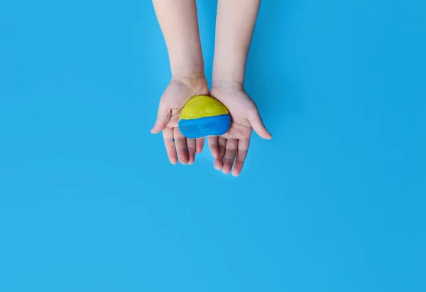Children\'s hands hold a stone painted in the colors of the Ukrainian flag. Conflict between the US, NATO and Russia in Ukraine. Stop the War in Ukraine 2022.