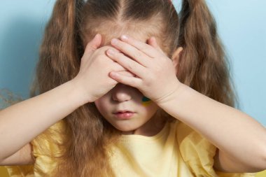 Ukrayna bayrağının arka planında üzgün bir kız çocuğu. Küçük Ukraynalı vatansever, ülkedeki savaş yüzünden ağlıyor..