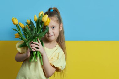 Ukrayna bayrağının arka planında şirin bir kız çocuğu bir buket sarı lale çiçeği tutuyor. sarı mavi arkaplan