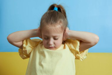 Korkmuş kız çocuğu savaştan korkuyor. Elleriyle kulaklarını kapatıyor ve savaşı durdurmak için elleriyle gösteriyor. Ukrayna bayrağının sarı-mavi arka planında