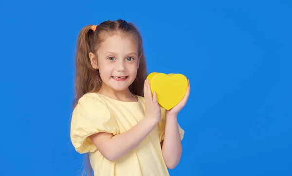 Menina Bonito Segurando Coração Amarelo Suas Mãos Fundo Azul Sorriso — Fotografia de Stock