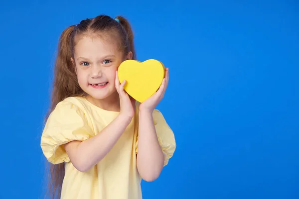 Menina Bonito Segurando Coração Amarelo Suas Mãos Fundo Azul Sorriso — Fotografia de Stock