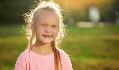 Kıç suratlı çocuk. Dişsiz gülüşü olan tatlı küçük kız. İlk süt dişi düştü. Gün batımında parkta gülümseyen çocuk