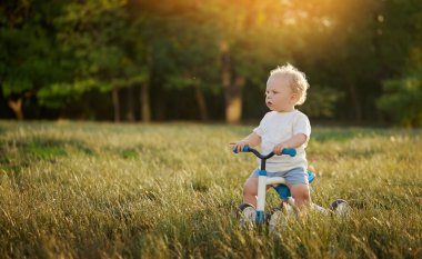 Sevimli bebek dengeli bisiklete binmeyi öğreniyor. Küçük bir çocuk güneşli bir parkta bisiklet sürmeye çalışır. Çocuk motosikletçi olmayı hayal ediyor.
