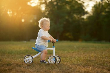 Sevimli bebek dengeli bisiklete binmeyi öğreniyor. Küçük bir çocuk güneşli bir parkta bisiklet sürmeye çalışır. Çocuk motosikletçi olmayı hayal ediyor.