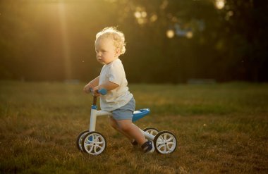 Sevimli bebek dengeli bisiklete binmeyi öğreniyor. Küçük bir çocuk güneşli bir parkta bisiklet sürmeye çalışır. Çocuk motosikletçi olmayı hayal ediyor.