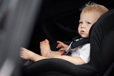 Bebek koltuğundaki komik çocuk. Düşünceli çocuk arabada oturur. Yolcu güvenliği kavramı