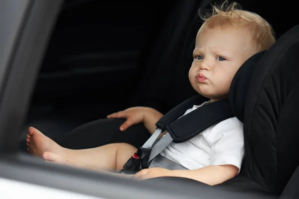 Funny baby boy in a car seat. Thoughtful child sits in the car. Passenger safety concept