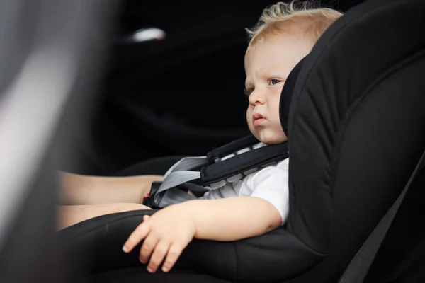 Funny baby boy in a car seat. Thoughtful child sits in the car. Passenger safety concept