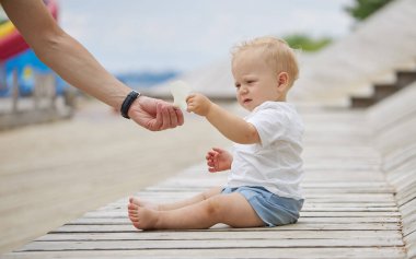 Dışarıda, çocuk parkında yerde oturan sevimli bir erkek bebek. Sevimli bebek yürümeyi öğreniyor. Sağlıklı fiziksel gelişim. Komik çocuk. Otantik yaşam tarzı, mutlu çocukluk..