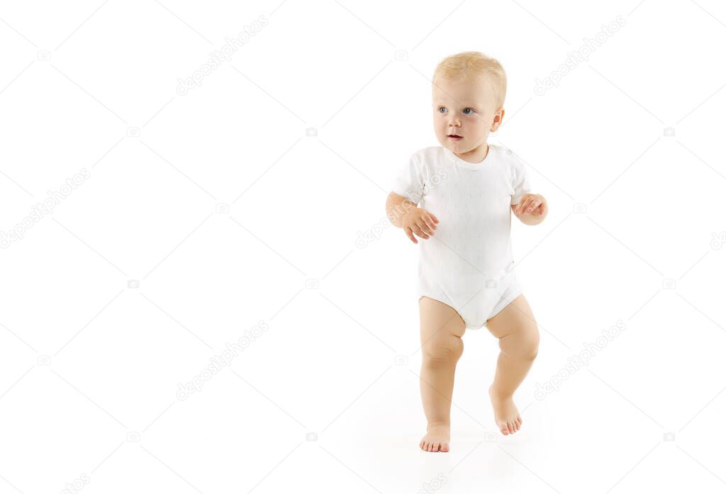 Cute baby learns to walk on a white isolated background. Happy smiling child in white clothes makes first confident steps