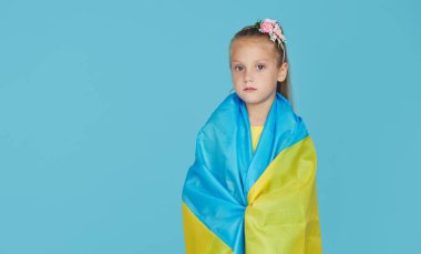 Mavi stüdyo arka planında Ukrayna bayrağı olan üzgün vatansever kız çocuğu portresi