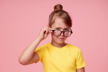 Pembe arka planda gözlüklü, sarı elbiseli akıllı kız başparmak gösteriyor. Çocuk eğitimi konsepti