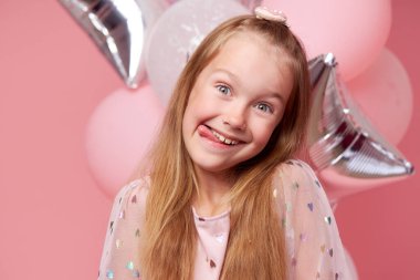 Balonların yanında zarif tül elbiseli neşeli kız çocuğu. Doğum günü hediyesi. Komik surat pembe arka planda doğum günü partisini kutluyor