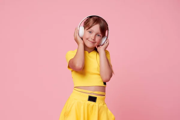 穿着黄色衣服的小女孩在粉色的背景上摆出一副很滑稽的姿势 模拟复制空间 用耳机听音乐 — 图库照片