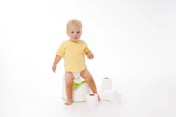 Potty training a baby. Little boy sitting on a potty next to a roll of toilet paper and diapers on a white background