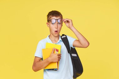 Gözlüklü, ders kitapları ve sarı arka planda sırt çantası olan bir okul çocuğunun portresi. Okula geri dön.