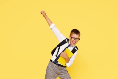 School break. Cheerful mischievous schoolboy in uniform with a backpack jumps on a yellow background. Beginning of holidays. Back to school. 