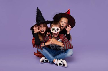 Mor arka planda Cadılar Bayramı onuruna karnaval kostümlü komik çocuklar..