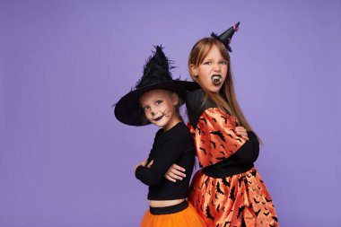 İskelet ve cadıdan oluşan karnaval kostümlü komik çocuklar mor arka planda Cadılar Bayramı onuruna.