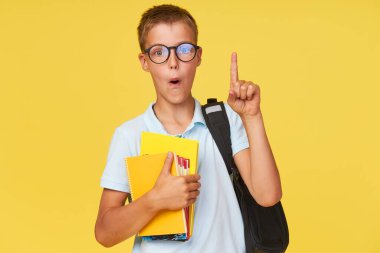 Ders kitaplarıyla gözlüklü bir okul çocuğunun portresi ve sarı arka planda baş parmağını gösteren bir sırt çantası. Okula geri dön.