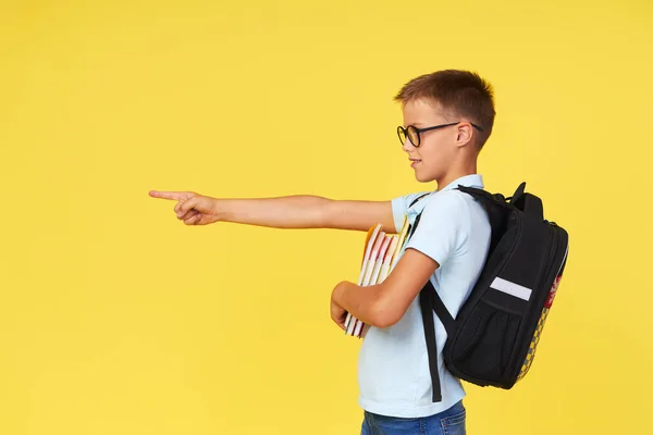 Portrait Schoolboy Glasses Textbooks Backpack Yellow Background Pointing Left Back — Stockfoto
