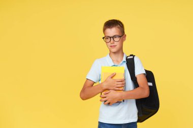 Gözlüklü, ders kitapları ve sarı arka planda sırt çantası olan bir okul çocuğunun portresi. Okula geri dön.