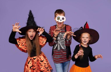 Mor arka planda Cadılar Bayramı onuruna karnaval kostümlü komik çocuklar..