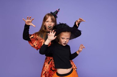 İskelet ve cadıdan oluşan karnaval kostümlü komik çocuklar mor arka planda Cadılar Bayramı onuruna.