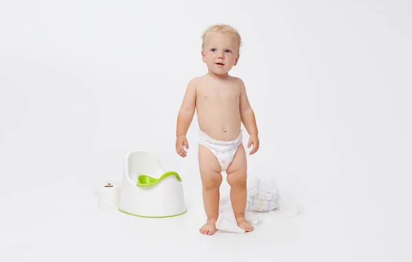 Potty training a baby. Little boy sitting on a potty next to a roll of toilet paper and diapers on a white background