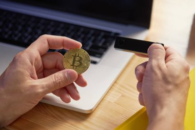 A young male freelancer works remotely in a cafe on a laptop and holds a crypto wallet in his hands