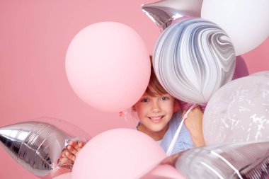 Balonların yanında zarif tül elbiseli neşeli kız çocuğu. Doğum günü hediyesi. Komik surat pembe arka planda doğum günü partisini kutluyor