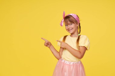 Sarı arka planda küçük şirin kız çocuğunun şaşırmış portresi. Kameraya bakıyorum. Ellerini yana doğru uzat. Çocuk ürünlerinin reklamını yapmak.