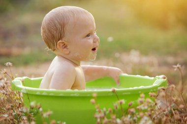 A small child plays in a bowl of water in a summer garden on a sunny day