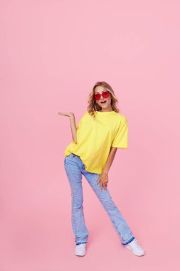 Full length portrait of a joyful young woman in casual clothes  on a pink background. Pointing to the left. Copy space