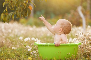 A small child plays in a bowl of water in a summer garden on a sunny day