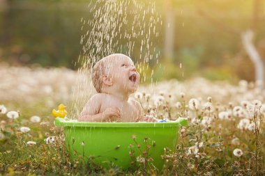 A small child plays in a bowl of water in a summer garden on a sunny day