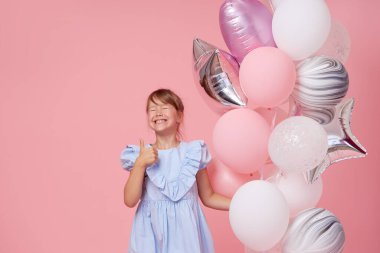 Balonların yanında zarif tül elbiseli neşeli kız çocuğu. Doğum günü hediyesi. Komik surat pembe arka planda doğum günü partisini kutluyor