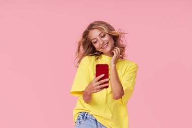 A young girl communicates via video communication on a smartphone on a pink background. Online chatting and blogging. Selfie on mobile phone camera smartphone