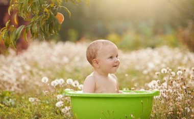 A small child plays in a bowl of water in a summer garden on a sunny day