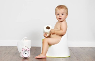 Cute baby boy sits on the potty with toilet paper in his hands. Potty training time