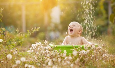 A small child plays in a bowl of water in a summer garden on a sunny day